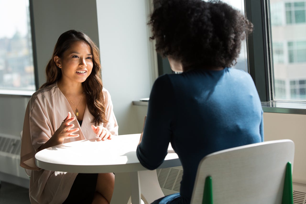 Two women sitting at a table having a professional discussion in a bright office setting
